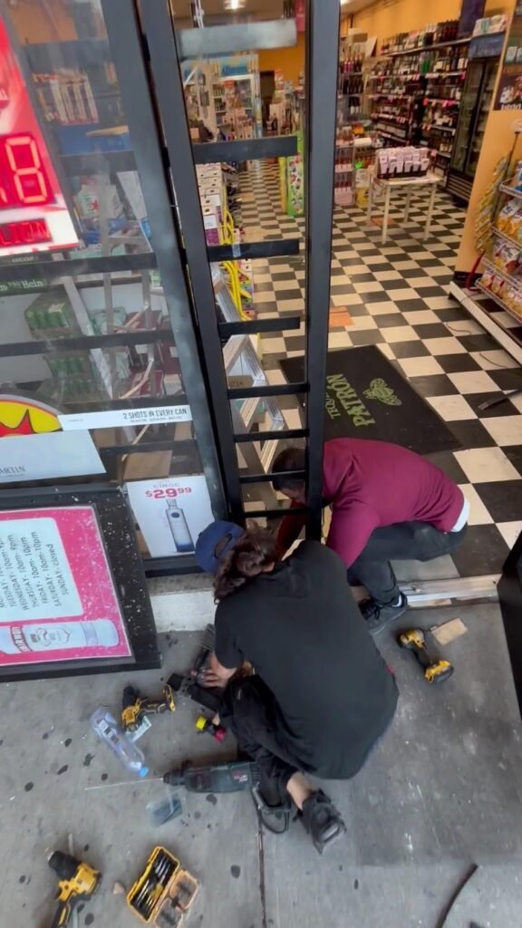Two technicians repairing a glass storefront door at a convenience store