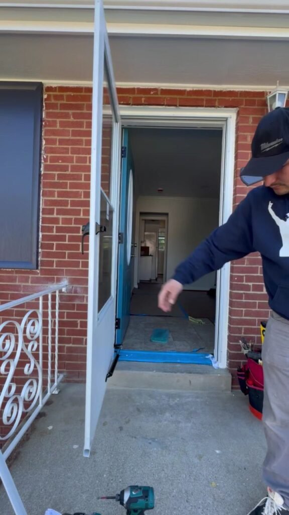 Technician working on a glass storm door at a brick home